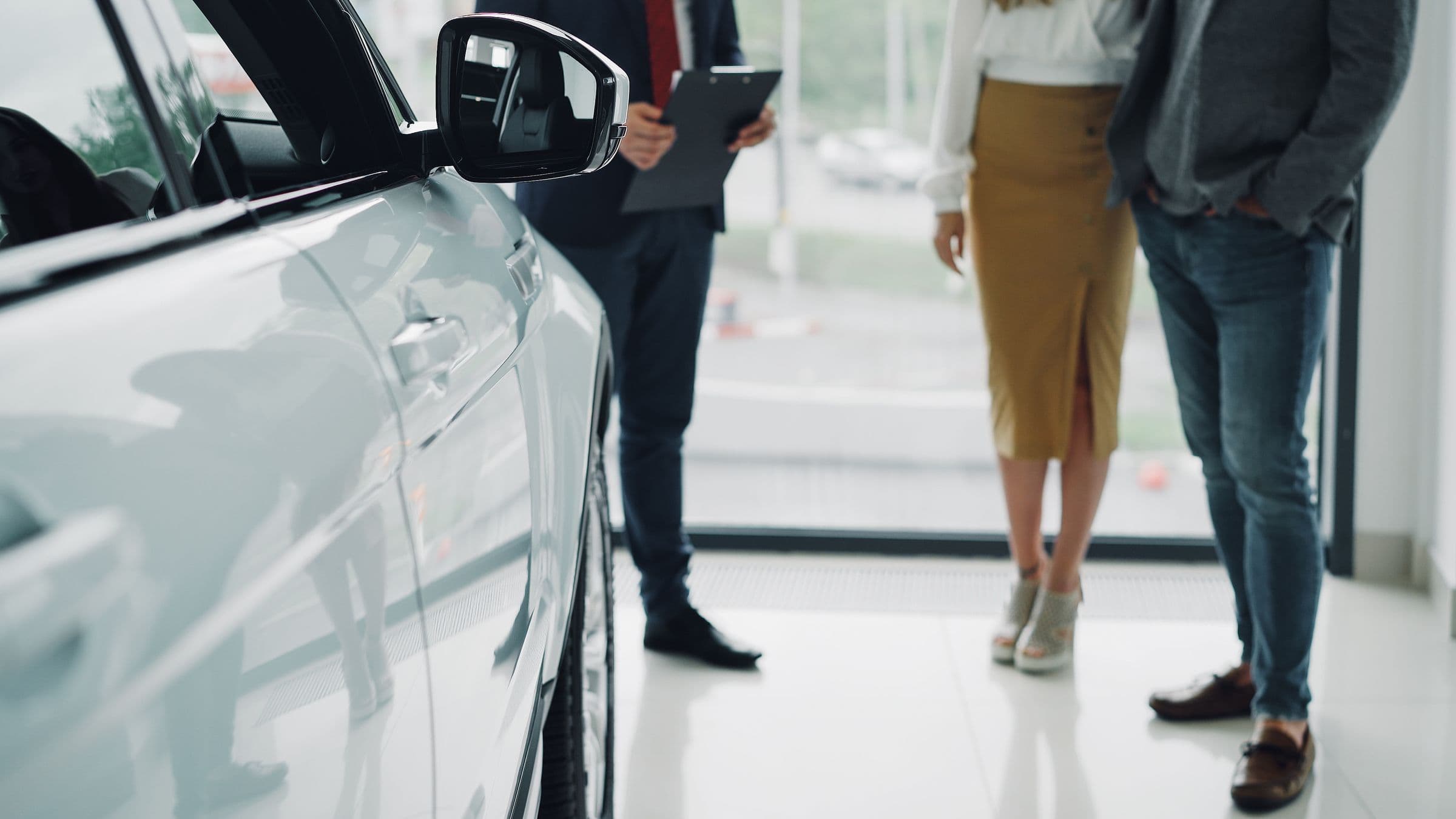 An advisor consulting a couple beside a car in a bright dealership showroom