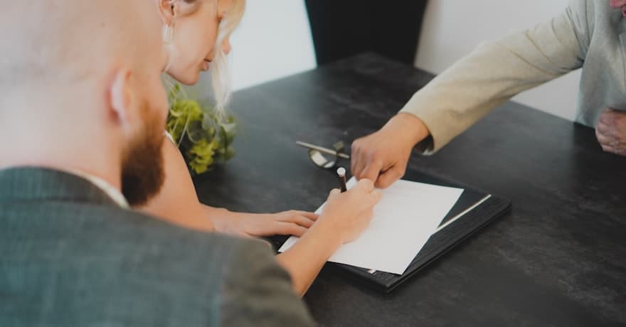A borrower signing mortgage paperwork with an advisor across the desk