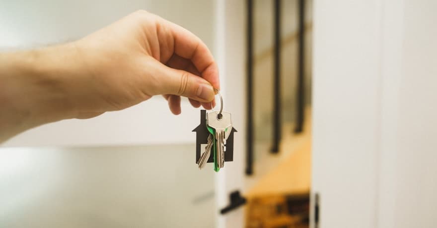 A hand holding house keys on a house-shaped keyring in a doorway