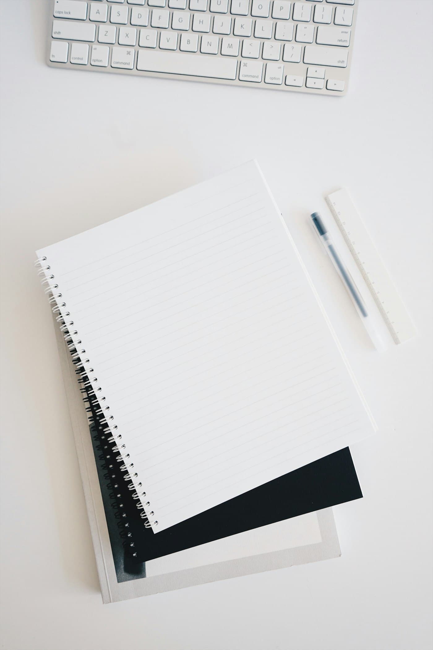 A notebook, pen and keyboard laid out on a desk